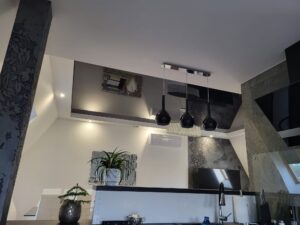 Sufit napinany w aneksie kuchennym – dwukolorowy z lampami wiszącymi (Radom) Dwukolorowy sufit napinany w aneksie kuchennym – matowa biała obwódka i grafitowy połysk, czarne lampy wiszące – realizacja ABOR serwis Radom