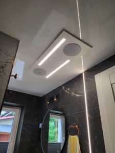 Sufit napinany w łazience z pionową linią świetlną LED (Radom) Sufit napinany w łazience z podświetlanym panelem i efektowną, pionową linią świetlną LED na tle czarnego marmuru – realizacja ABOR serwis Radom